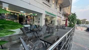 An outdoor seating area with tables and chairs, a glass storefront, and a building facade with windows and decorative elements.