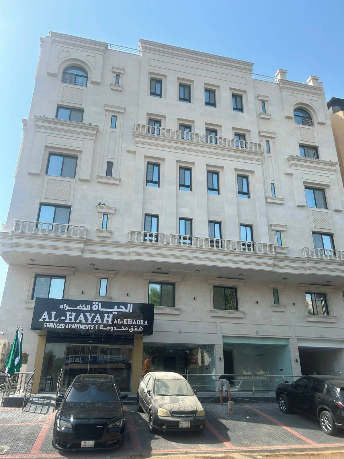 A multi-story building with a sign for 'AL-HAYAH KHADRA Serviced Apartments'.