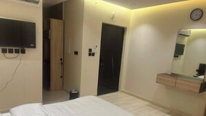 A hotel room with a bed, a TV mounted on the wall, a mirror above the dresser, and a door leading to another room.