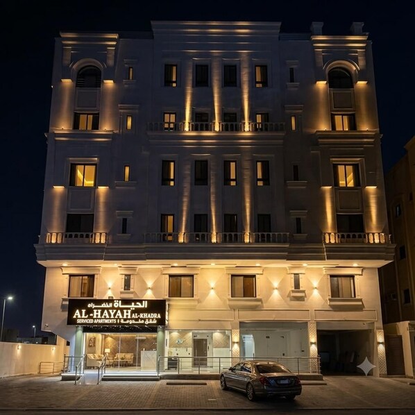 A multi-story building with illuminated windows and a sign for serviced apartments.