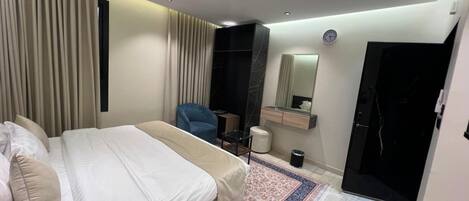 A modern bedroom with a bed, a chair, a small table, a mirror, and a door.