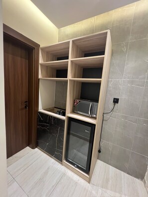 Una habitación con estantería empotrada de madera, microondas y refrigerador.