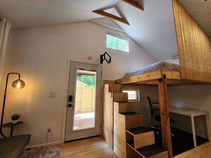 A room with a bunk bed, a desk, a chair, a lamp, and a door leading outside. - Unique Cotswold Guesthouse Near Hospitals. Pet Friendly (Charlotte)