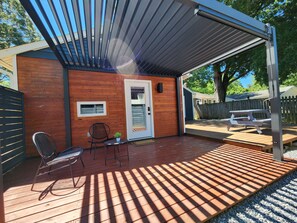 A covered patio with a wooden deck, a door, and a small table with chairs. - Unique Cotswold Guesthouse Near Hospitals. Pet Friendly (Charlotte)