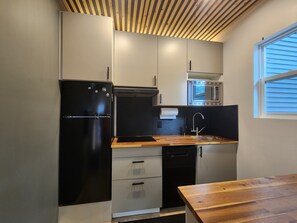 Eine kleine Küche mit einem schwarzen Kühlschrank, einer Mikrowelle und einer Holzausziehtafel.