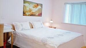 Un dormitorio con cama, un cuadro en la pared, una ventana con persianas y un escritorio con silla.