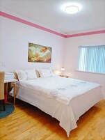 Um quarto com uma cama, um quadro na parede, uma janela com persianas e uma escrivaninha com uma cadeira.