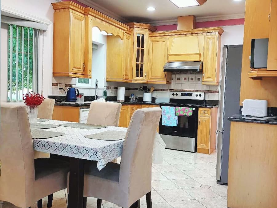 Una cocina con armarios de madera, una mesa de comedor con sillas y suelo de baldosas.