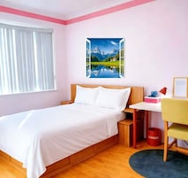 Quarto com cama, escrivaninha, cadeira, janela com persianas e um quadro de paisagem.