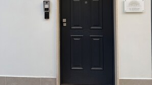 Una porta nera con un piccolo oblò sopra, una cassetta postale e una targa appesa al muro.