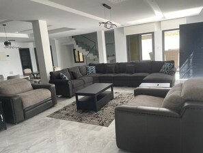 Una sala de estar moderna con un sofá modular, sillones, una mesa de centro y una escalera al fondo.