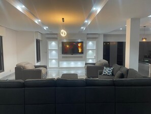 A modern living room with a sectional sofa, a flat-screen TV, recessed lighting, and a minimalist design.