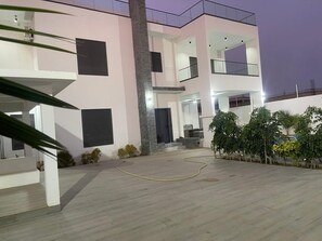 A modern multi-story building with a flat roof, balconies, and a paved courtyard.