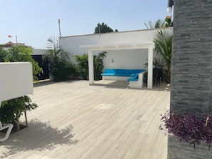 Un espacio patio al aire libre con un sofá azul, rodeado de plantas en macetas y una estructura de pared blanca.