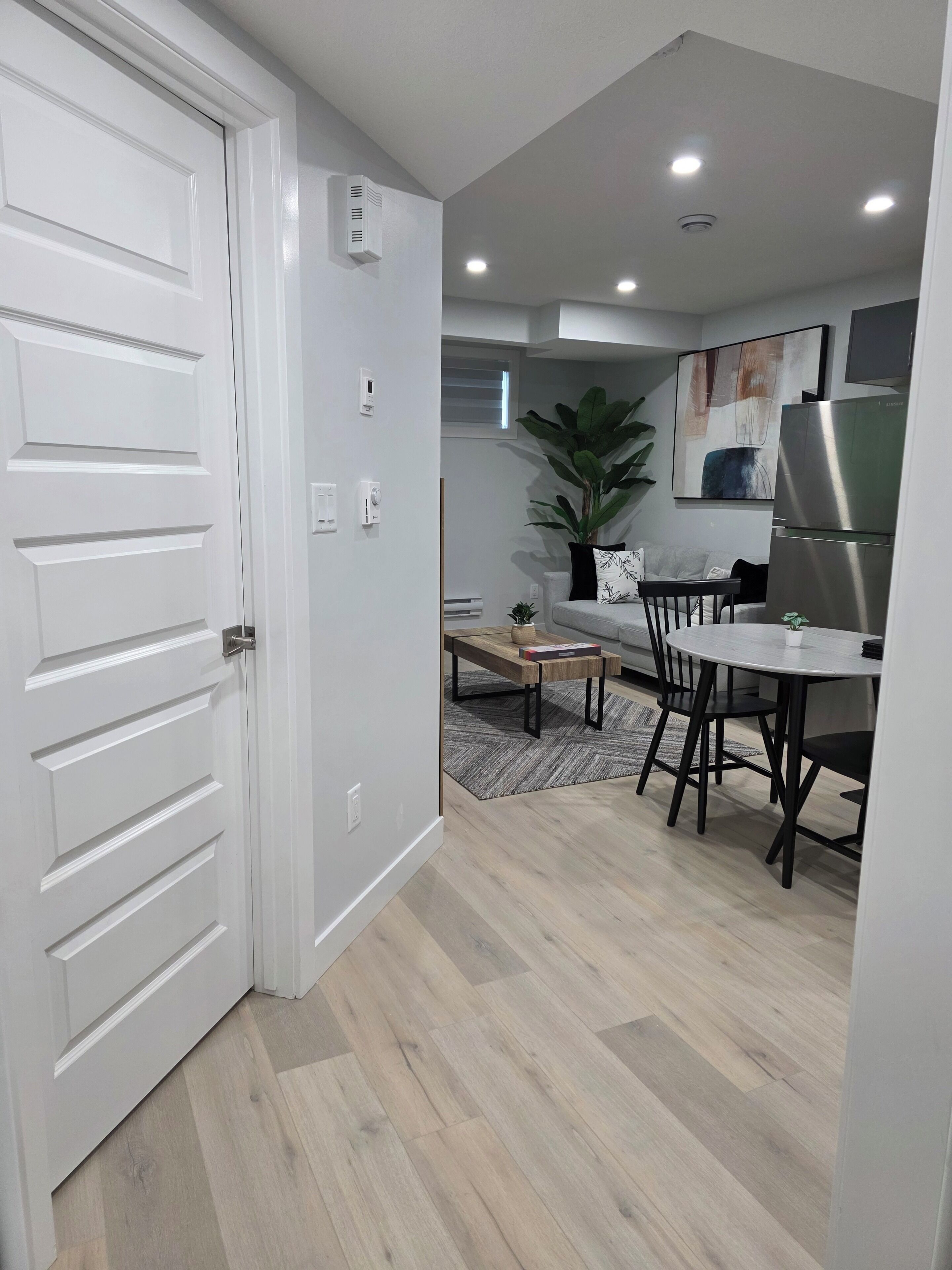 A modern kitchen with a dining area, white cabinetry, and a large plant.