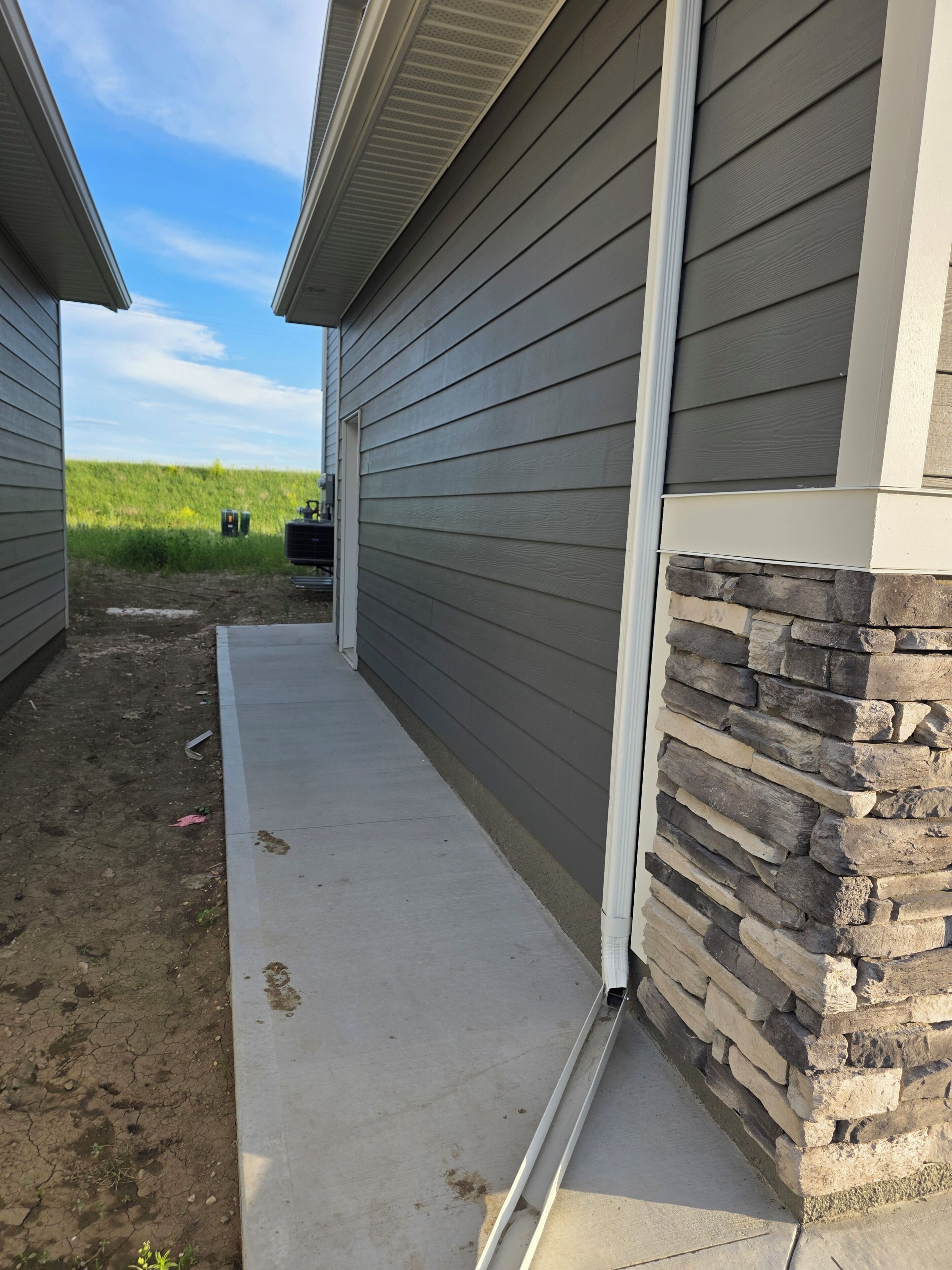 A building with a stone accent wall, a concrete pathway, and a grassy field in the background.