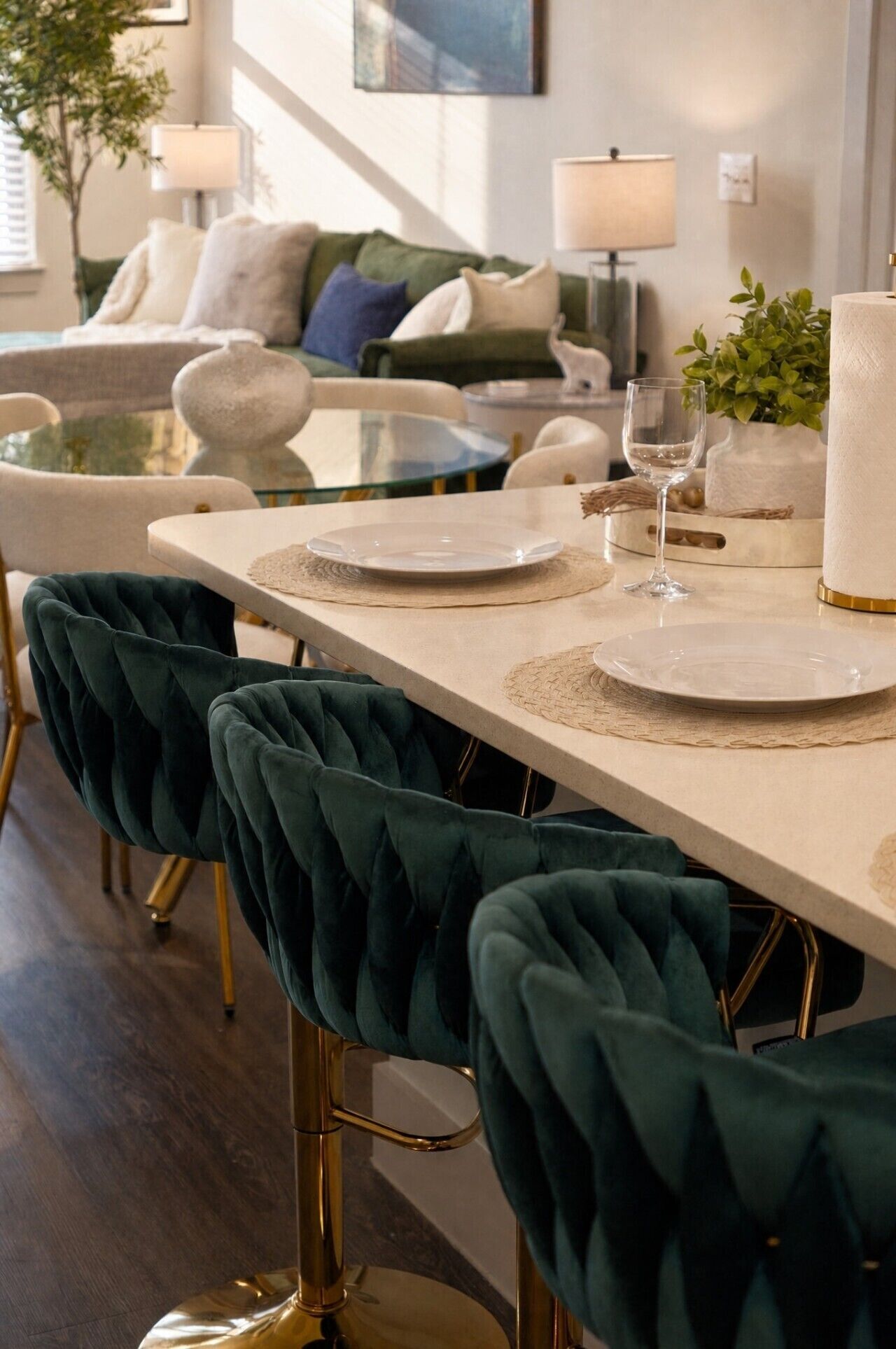 A dining area with a long table, two chairs, a glass-top table, and a potted plant.