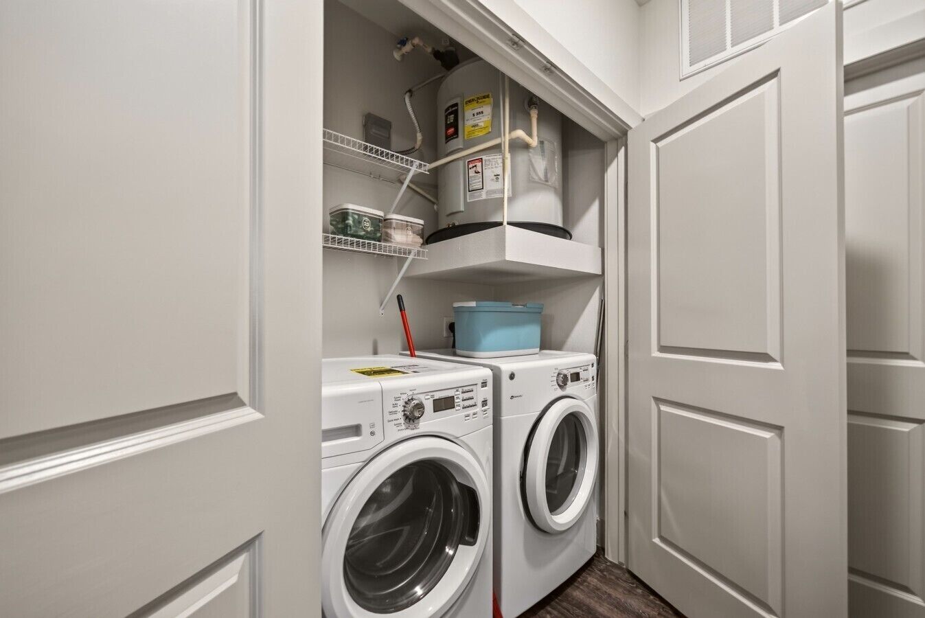 A laundry room with two front-loading washing machines, a shelf with folded clothes, and a blue laundry basket.