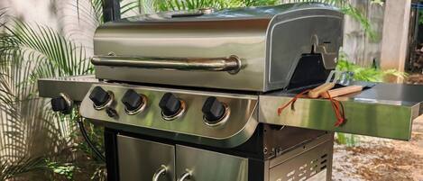 Un barbecue extérieur en acier inoxydable, doté de quatre brûleurs, d’un brûleur latéral et d’un four intégré, installé sur une pelouse artificielle.