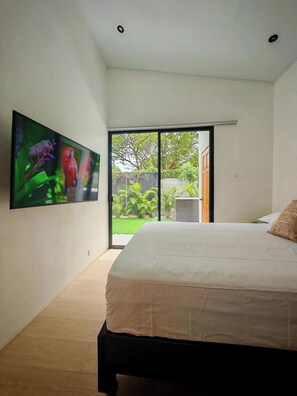 Un dormitorio con cama, televisor en la pared y puerta corrediza de vidrio que da a un jardín.