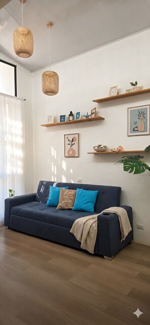 A modern living room with a dark blue sofa, two hanging wicker lamps, and wooden shelves with decorative items.
