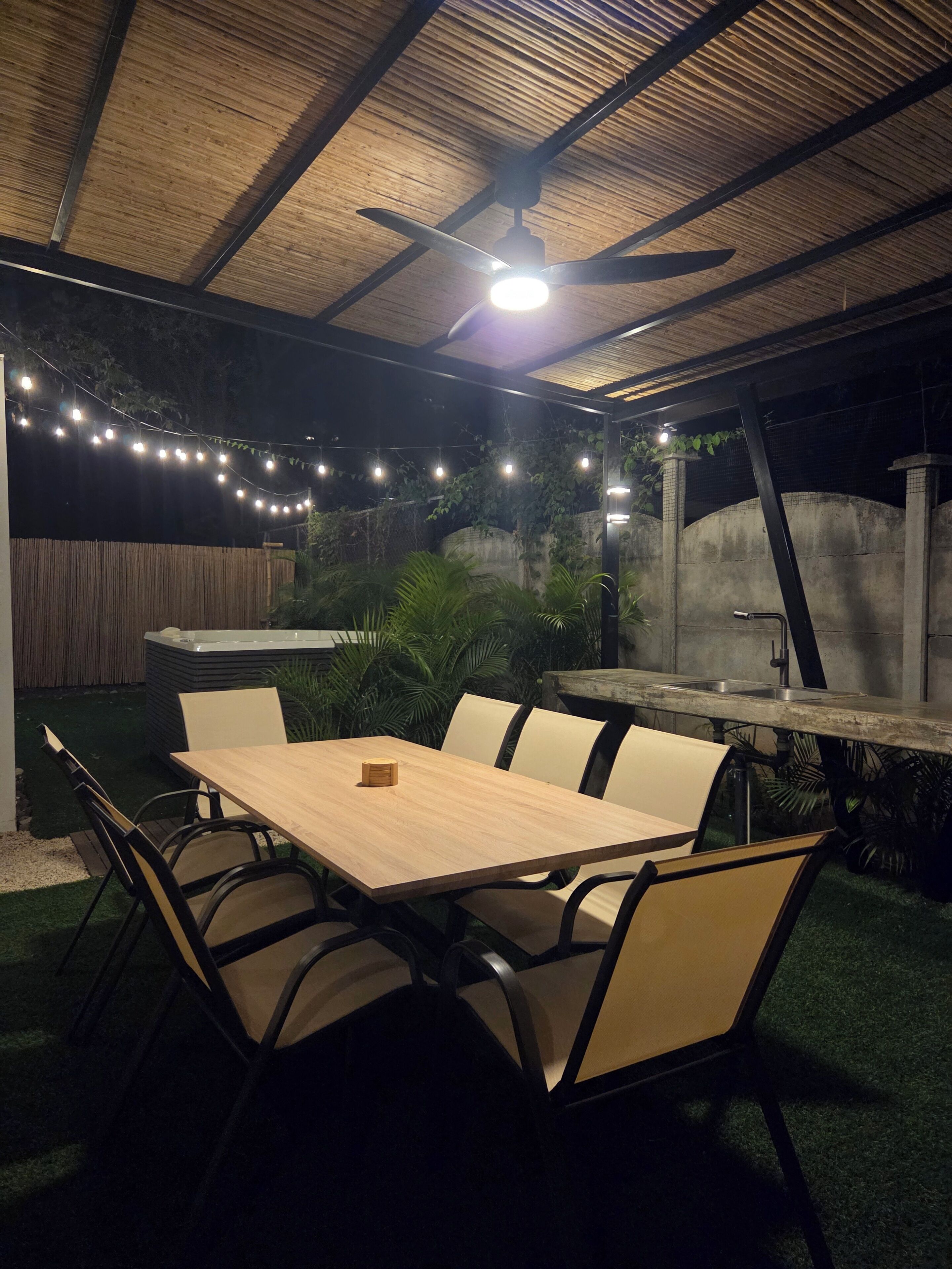 An outdoor patio with a table and chairs, a ceiling fan, and string lights.