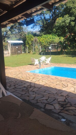 A swimming pool with stone tiles, surrounded by a grassy area and trees.