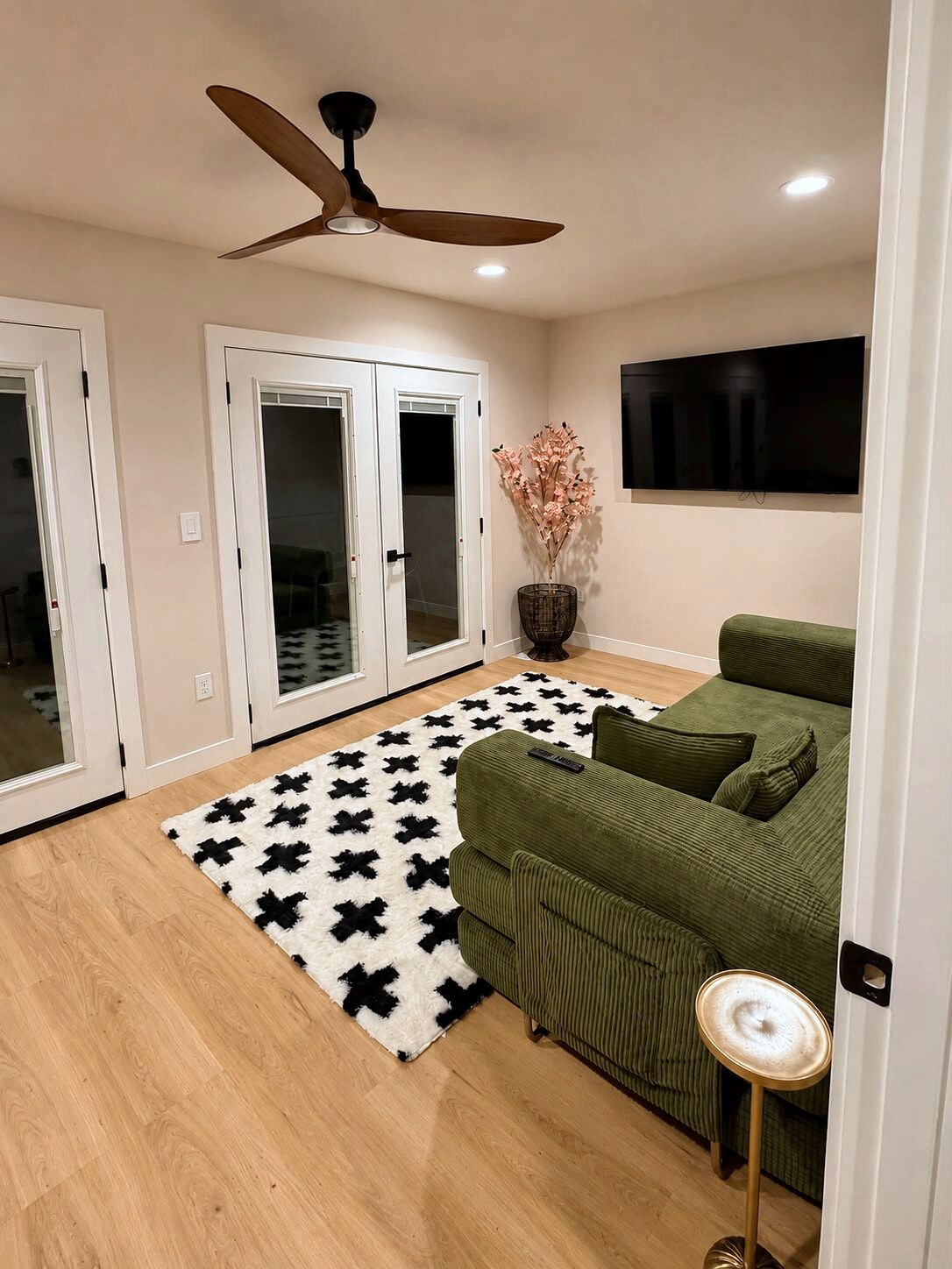 A room with a ceiling fan, a green sofa, a patterned rug, and a television on the wall.
