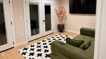 A room with a ceiling fan, a green sofa, a patterned rug, and a television on the wall.
