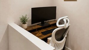 Et hjemmekontor med en computerbord, en stol, et fjernsyn og et billede i ramme på væggen.
