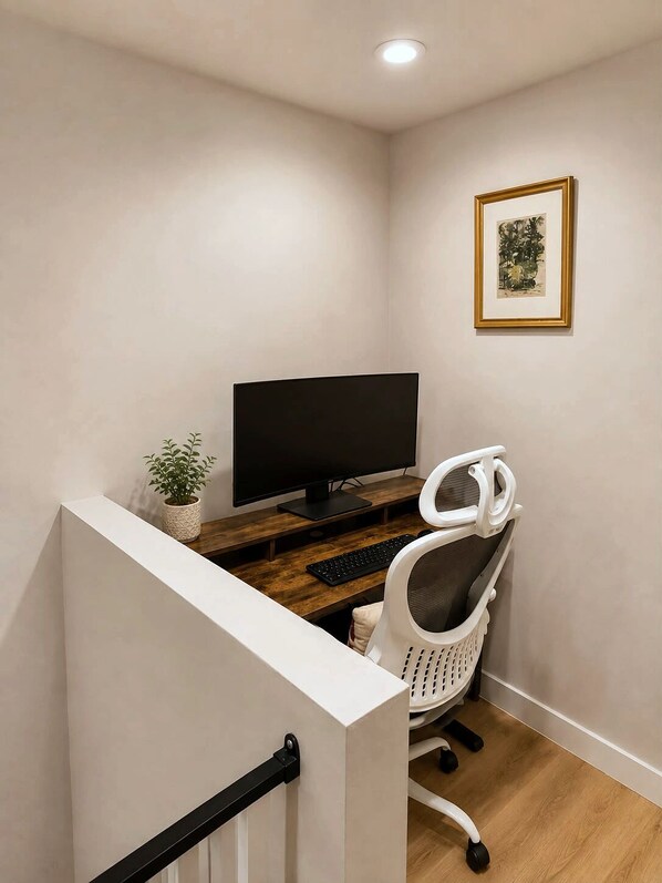 Ein Homeoffice mit Schreibtisch, Stuhl, Fernseher und einem gerahmten Bild an der Wand.