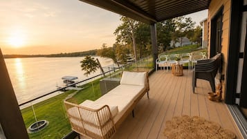 A balcony with a sofa, chairs, and a view of a body of water during sunset.