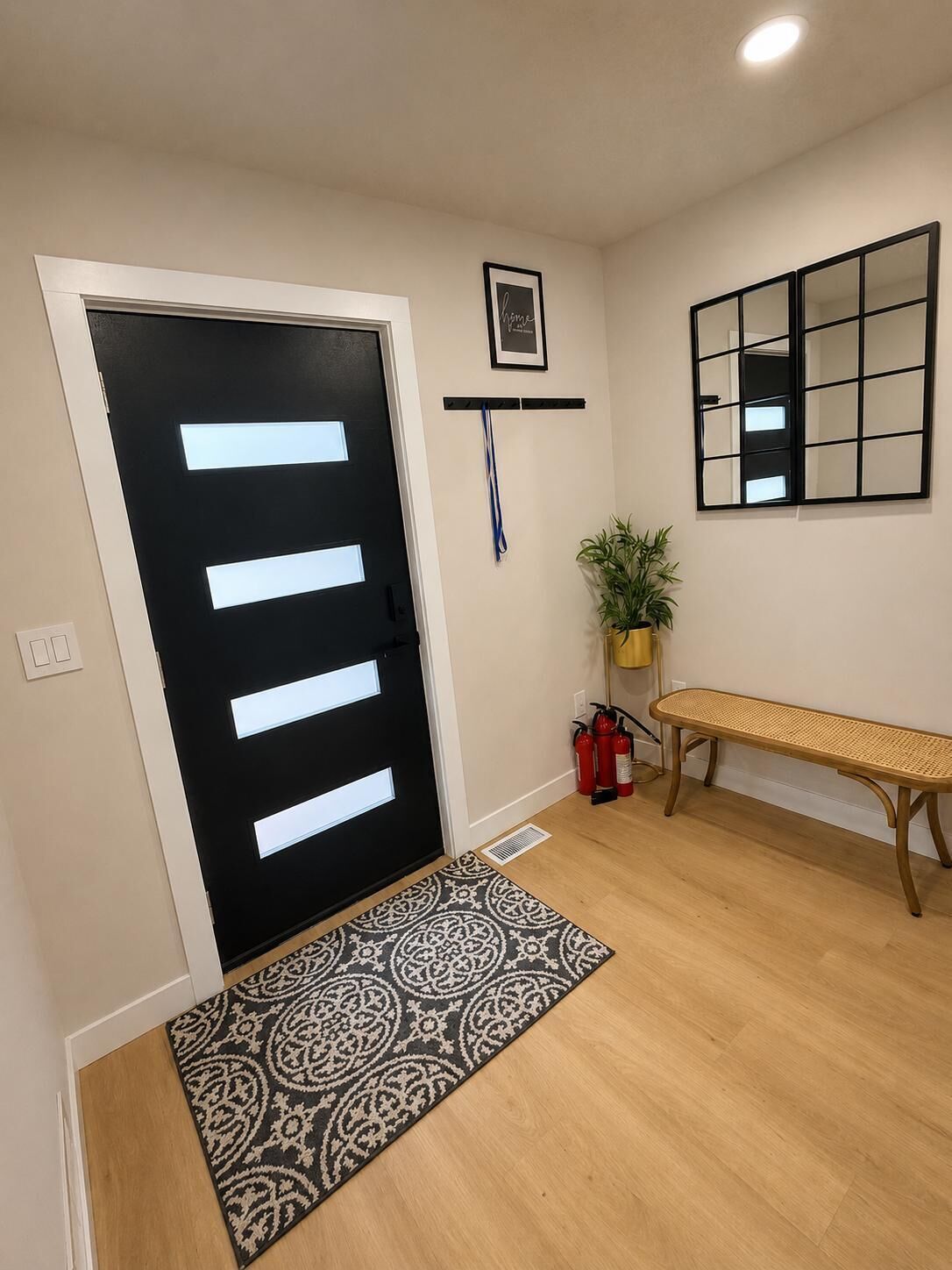 A hallway with a black door, a patterned rug, a bench, a plant, and a framed picture on the wall.