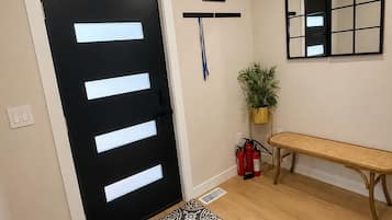 A hallway with a black door, a patterned rug, a bench, a plant, and a framed picture on the wall.