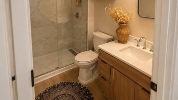 A bathroom with a glass-enclosed shower, a toilet, a sink with a mirror, and a decorative vase.