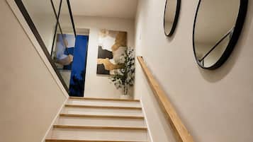 A staircase with wooden steps and a wooden handrail, leading to a landing with a wall-mounted mirror and a framed abstract painting.