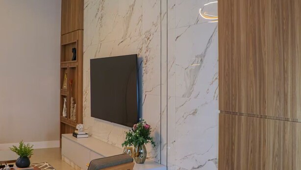 Una sala moderna con un televisor de pantalla plana montado en una pared de mármol, una estantería de madera, un sillón cómodo y una mesita con adornos.