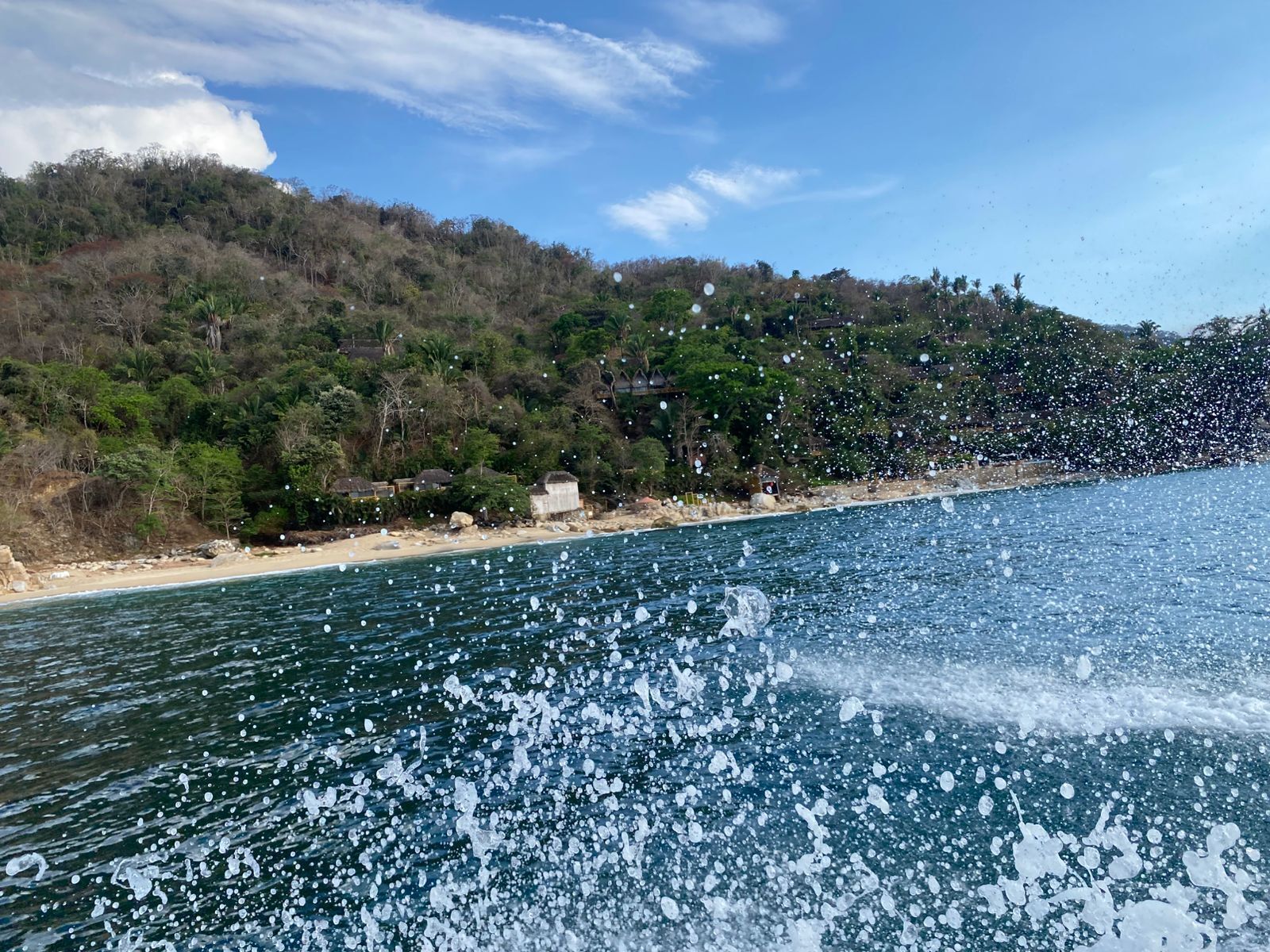 Paisagem costeira com praia, colina arborizada e céu claro.