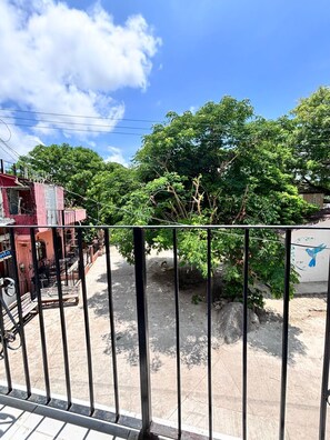 Un balcón con barandilla de metal que da a un patio con árboles y un edificio con un letrero.