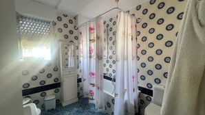 Kylpyhuone, jossa on suihkuverho, wc-istuin, pesuallas ja peili.