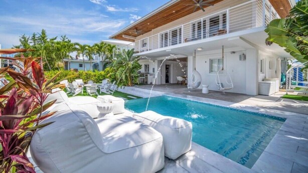 Uma casa moderna com piscina, área de estar externa e plantas tropicais.