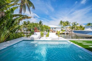 Ein Swimmingpool mit Liegestühlen, umgeben von tropischer Vegetation und einem klaren Himmel.
