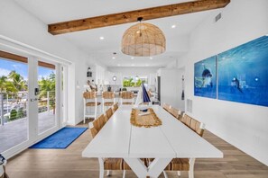A spacious dining area with a white table and wooden chairs, a large window with a view of palm trees, and a ceiling with exposed beams. - Private Beach, Waterfront, Islamorada, Island house with a pool & a boat dock (Islamorada)