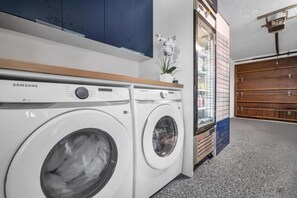 Een wasruimte met Samsung wasmachines, een blauwe kast en een houten deur.