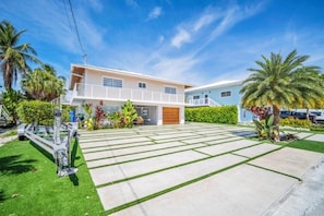 A two-story house with a driveway, palm trees, and a clear sky. - Private Beach, Waterfront, Islamorada, Island house with a pool & a boat dock (Islamorada)