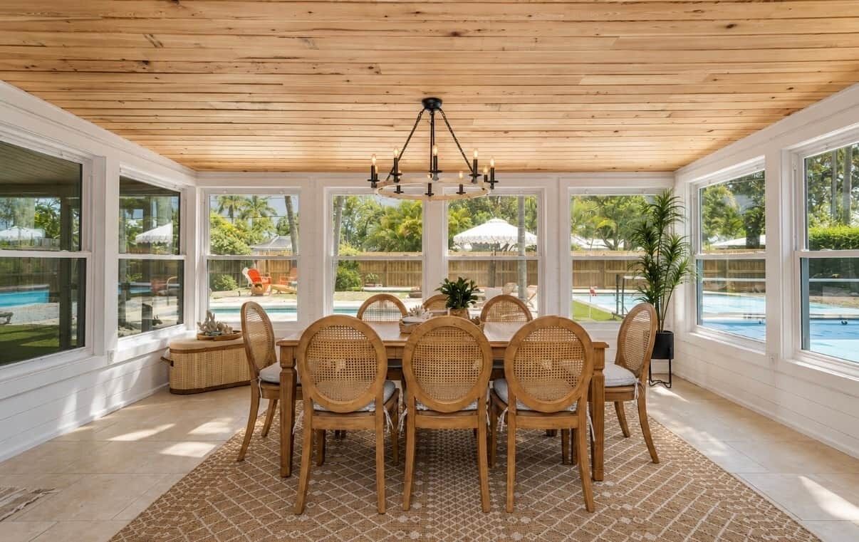 A covered dining area with a pool view, featuring a wooden ceiling, large windows, and a chandelier.