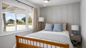 A bedroom with a wooden bed, two bedside lamps, a nightstand, and a window with curtains. - Coastal Cactus- Pool+Pickleball+Putting Green+Shuffleboard! (Manatee County)
