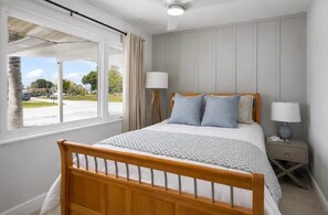 A bedroom with a wooden bed, two bedside lamps, a nightstand, and a window with curtains. - Coastal Cactus- Pool+Pickleball+Putting Green+Shuffleboard! (Manatee County)