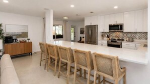 A modern kitchen with white cabinetry, a large island with bar stools, a refrigerator, a microwave, and a stove. - Coastal Cactus- Pool+Pickleball+Putting Green+Shuffleboard! (Manatee County)