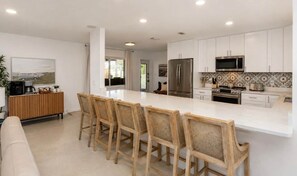 A modern kitchen with white cabinetry, a large island with bar stools, a refrigerator, a microwave, and a stove. - Coastal Cactus- Pool+Pickleball+Putting Green+Shuffleboard! (Manatee County)